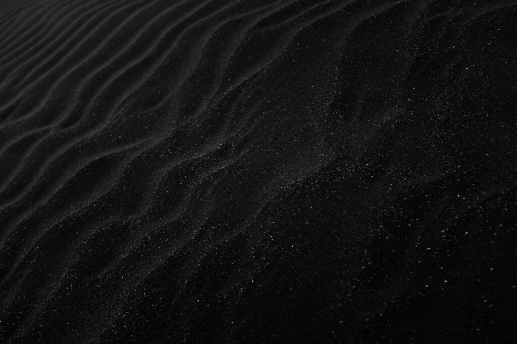 Textured black sand with ripples resembling dunes, creating a dark, abstract aesthetic.